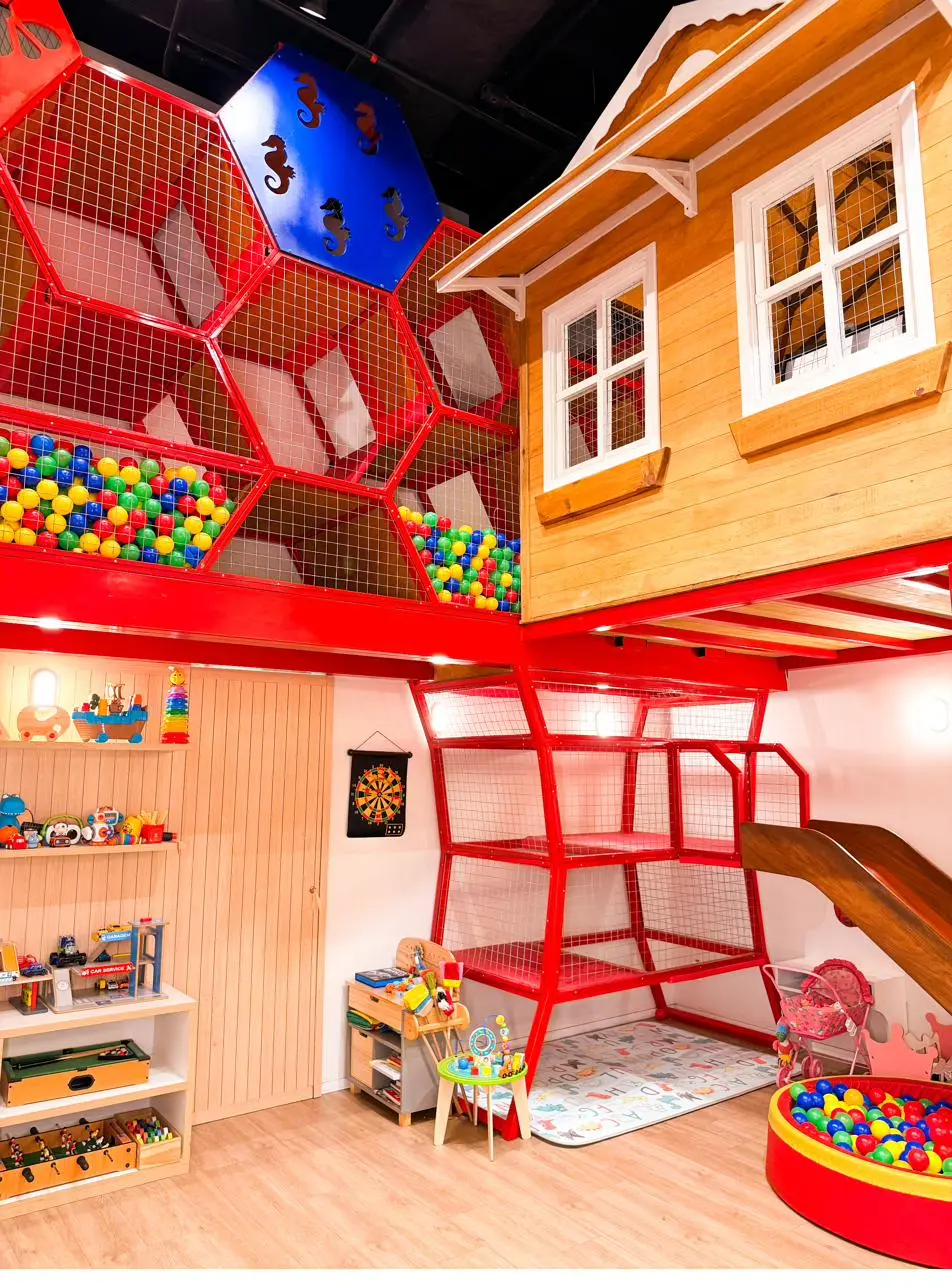 Casinha de madeira suspensa com escorregador e piscina de bolinhas em estrutura de hexágonos vermelhos, na brinquedoteca da Arte em Retalhos